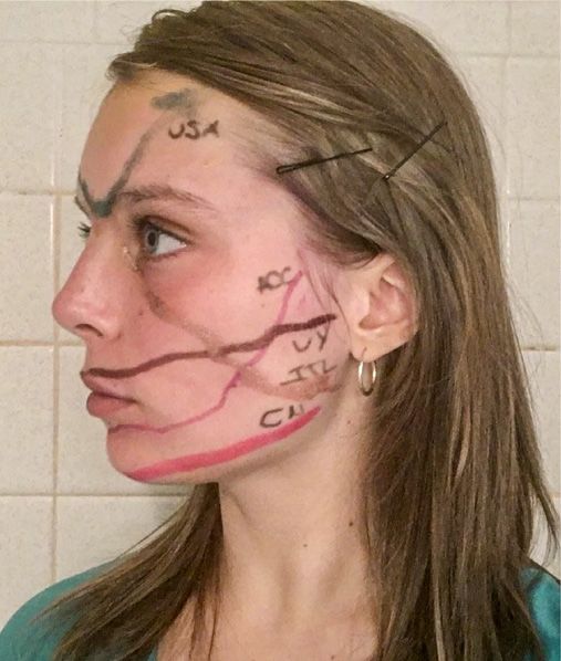Lines of red, yellow, green, bronze, and brown makeup criss-cross a teenage girl's face. The marks depict line graphs of Covid-19 cases in Spain, the United States of America, Georgia's Athens-Clarke County, Uruguay, Italy, and China.