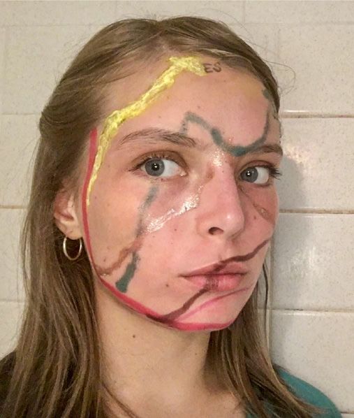 Lines of red, yellow, green, bronze, and brown makeup criss-cross a teenage girl's face. The marks depict line graphs of Covid-19 cases in Spain, the United States of America, Georgia's Athens-Clarke County, Uruguay, Italy, and China.