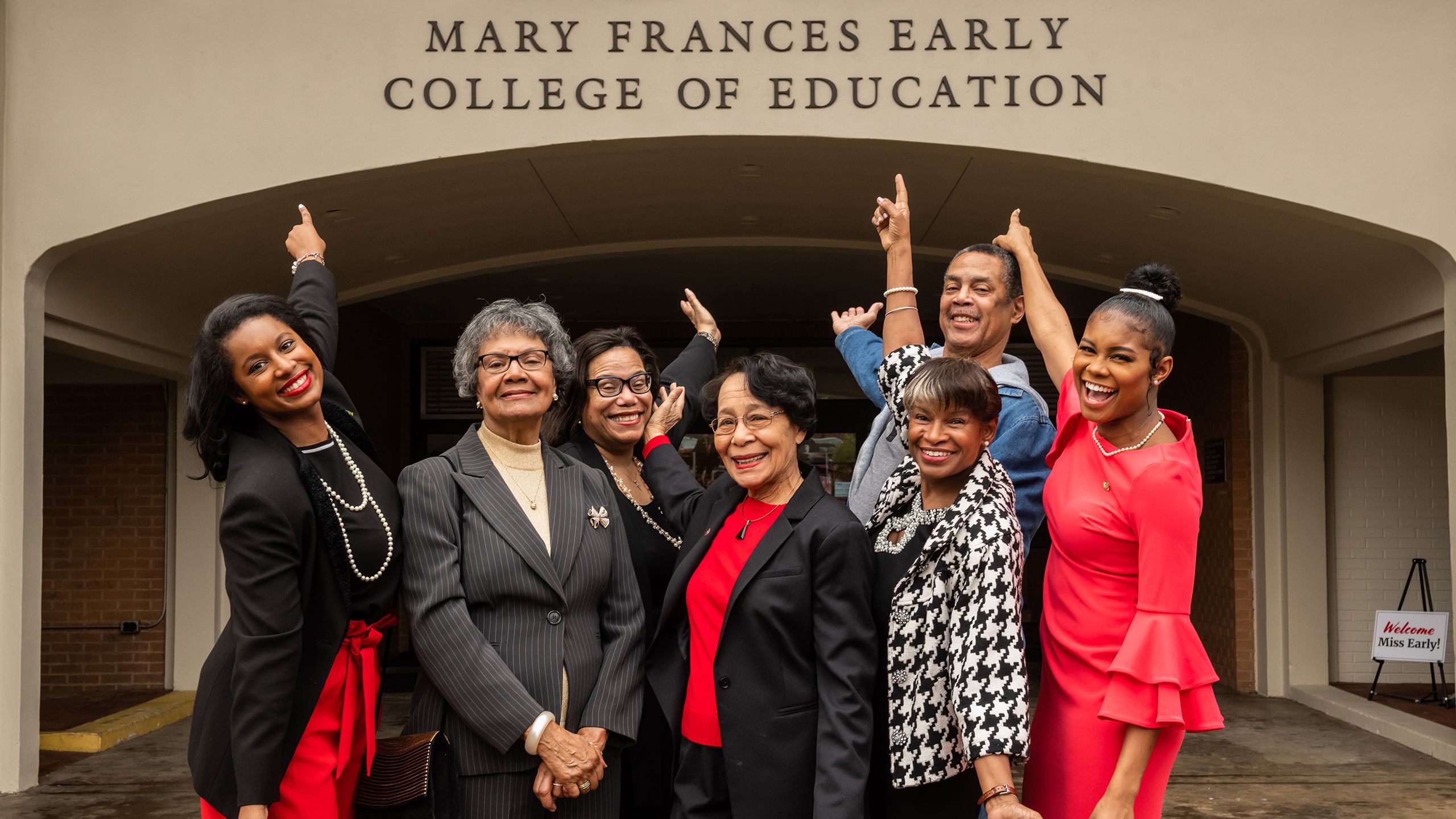 A group of Mary Frances Early's family members surround her as they point to the exterior sign bearing her name on Aderhold Hall