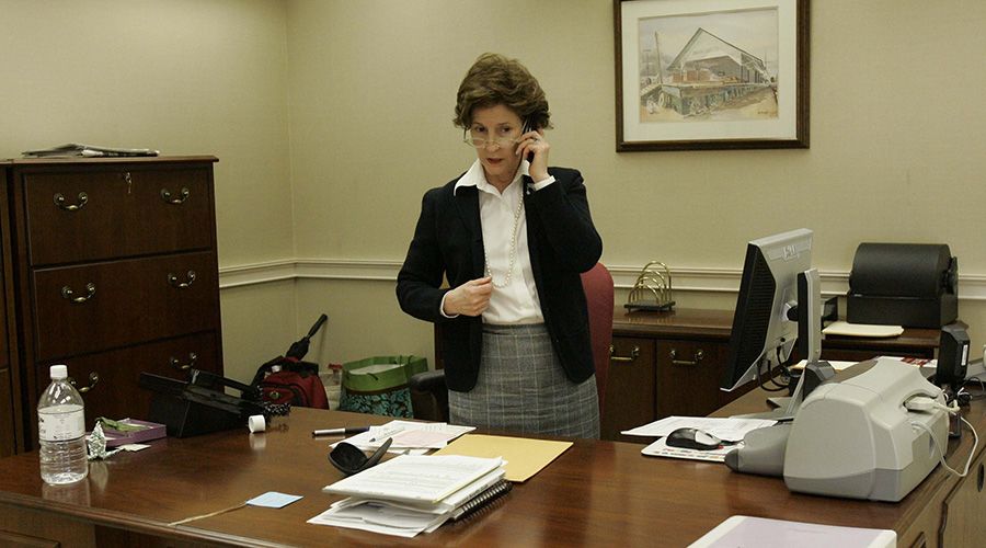 Inez Tenenbaum, glasses low on her nose, speaks intently on her cell phone in her office. Her desk is slightly cluttered with stacks of documents and a watercolor of a rural train depot hangs on the wall behind her.