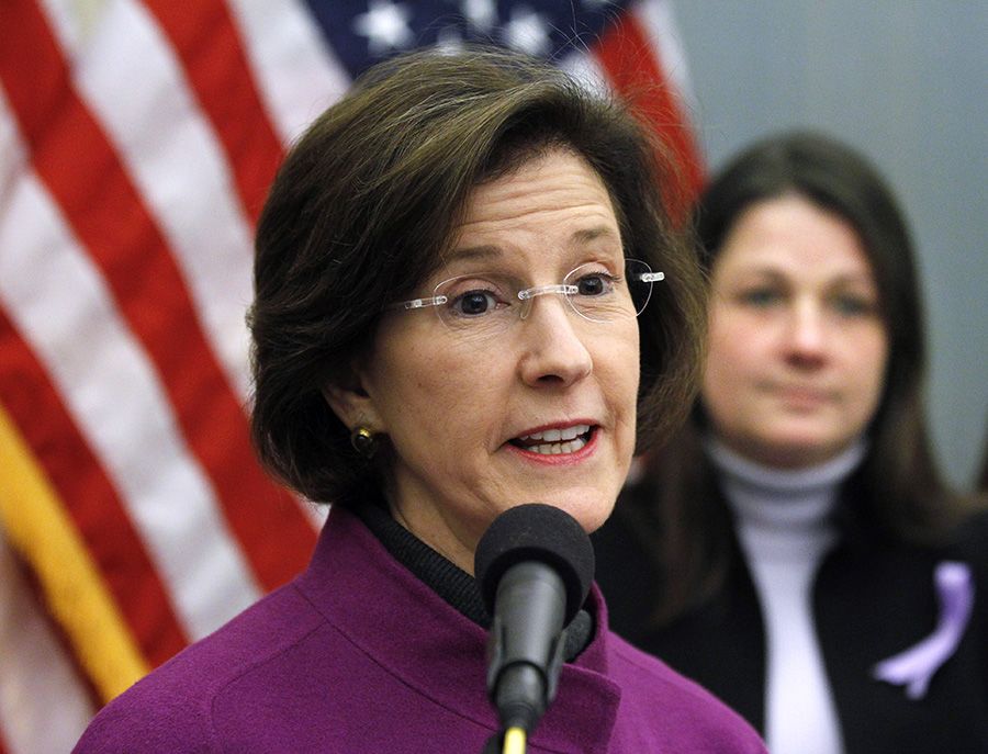Inez Tenenbaum speaks into a microphone in front of an American flag and a female onlooker at an event.